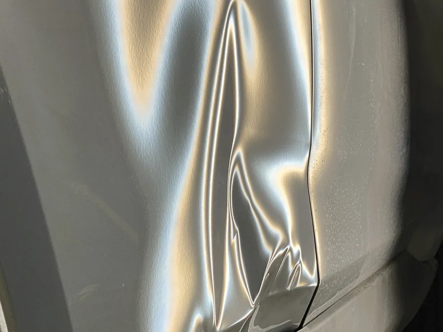 Sharp crease dent along the door and rear quarter panel of a silver vehicle at AUTOSTREAM360, seen under PDR reflector lighting before paintless repair